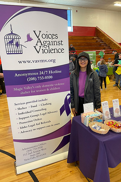 A smiling woman standing next to a sign for Voices Against Violence. Click to enlarge.