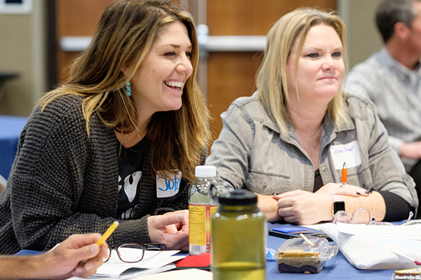 Two women smiling and laughing while speaking to others at their table. Click to enlarge.
