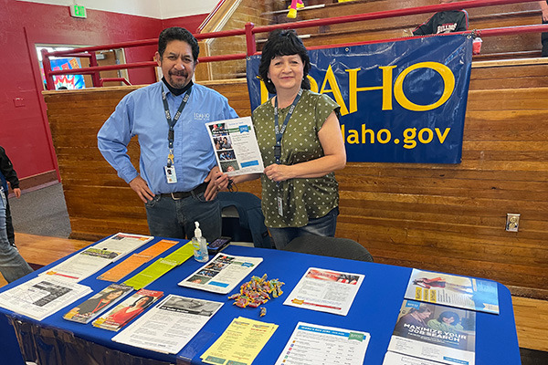 A smiling man and woman standing behind an Idaho Government information table. Click to enlarge.