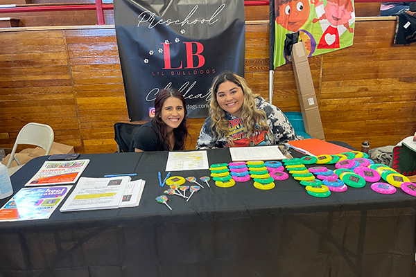 Two smiling women sitting behind a Lil Bulldogs preschool information table. Click to enlarge.